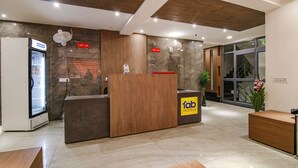 A hotel reception area with a wooden reception desk, a minibar, and a glass door leading to a staircase. - Fabhotel Moro Rohini Sector 4 (New Delhi)