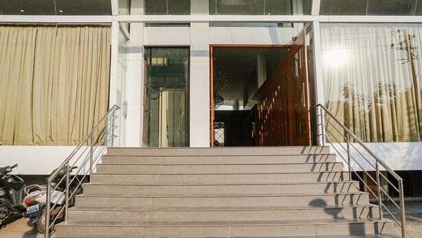A building entrance with a staircase leading up to a door, a motorcycle parked to the side, and a window with curtains. - Fabhotel Dreams Inn (Thane)