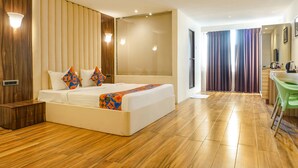 A modern hotel room with a large bed, wooden flooring, a small desk, and a bathroom visible through a glass door. - Fabhotel Dreams Inn (Thane)