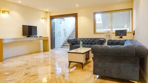 A modern living room with a flat-screen TV, a sofa, a coffee table, and a glass door leading to a staircase. - Fabhotel Dreams Inn (Thane)