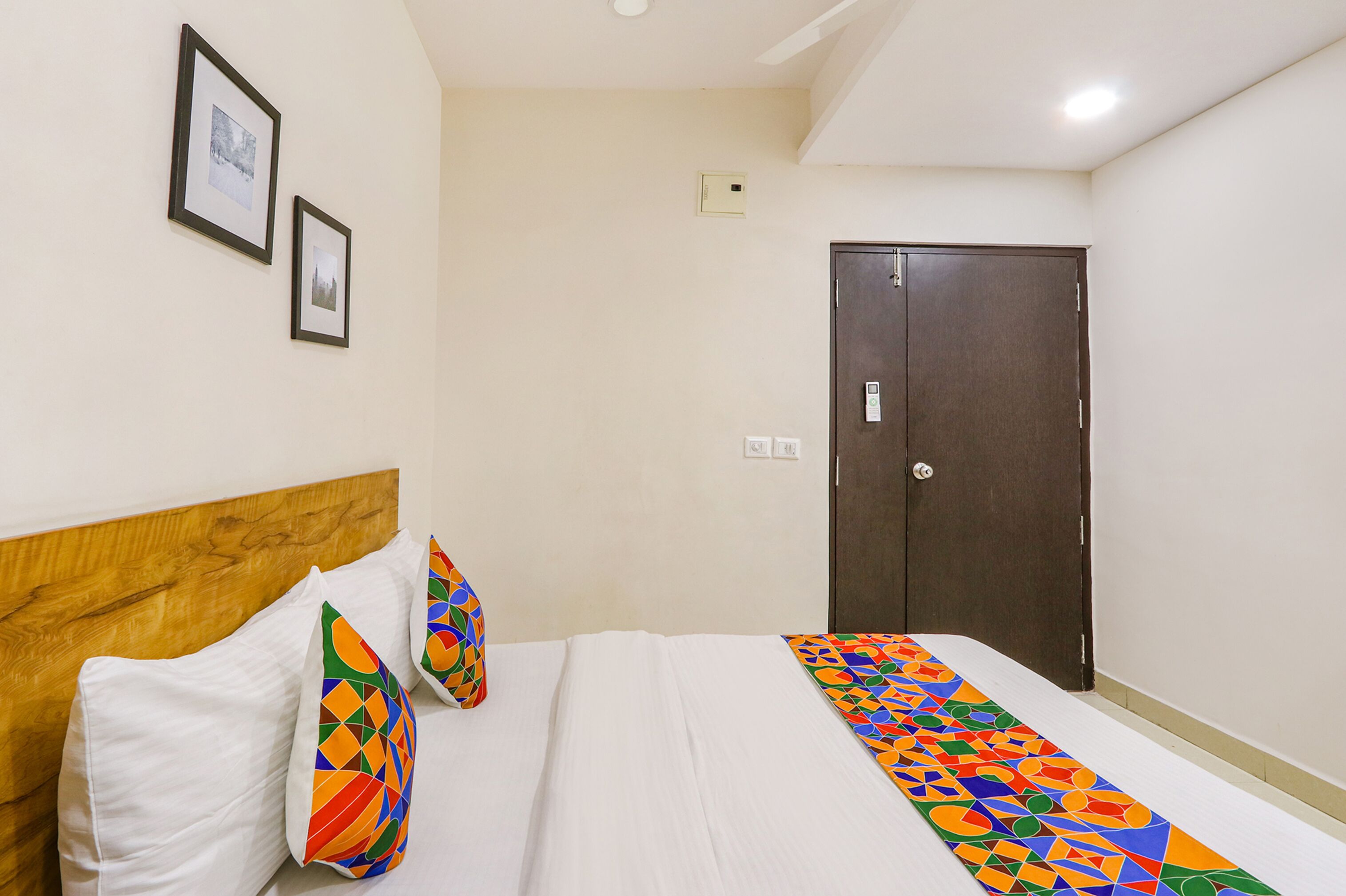 Una camera d'albergo con una testiera in legno, un letto con biancheria da letto bianca e cuscini colorati, un armadio in legno scuro e due quadri appesi alla parete.