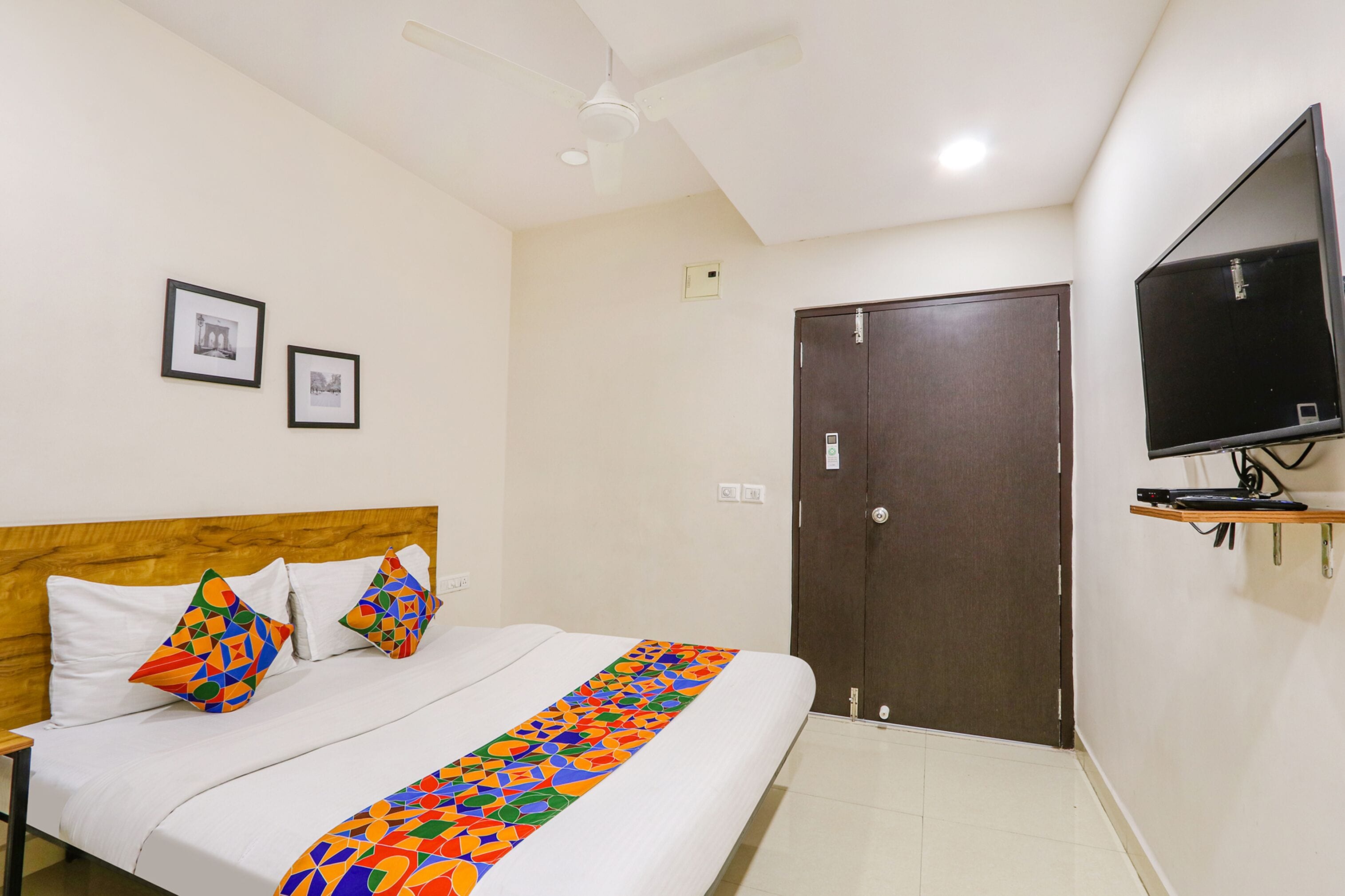 Une chambre d’hôtel avec un lit, un ventilateur de plafond, un téléviseur fixé au mur et une porte.