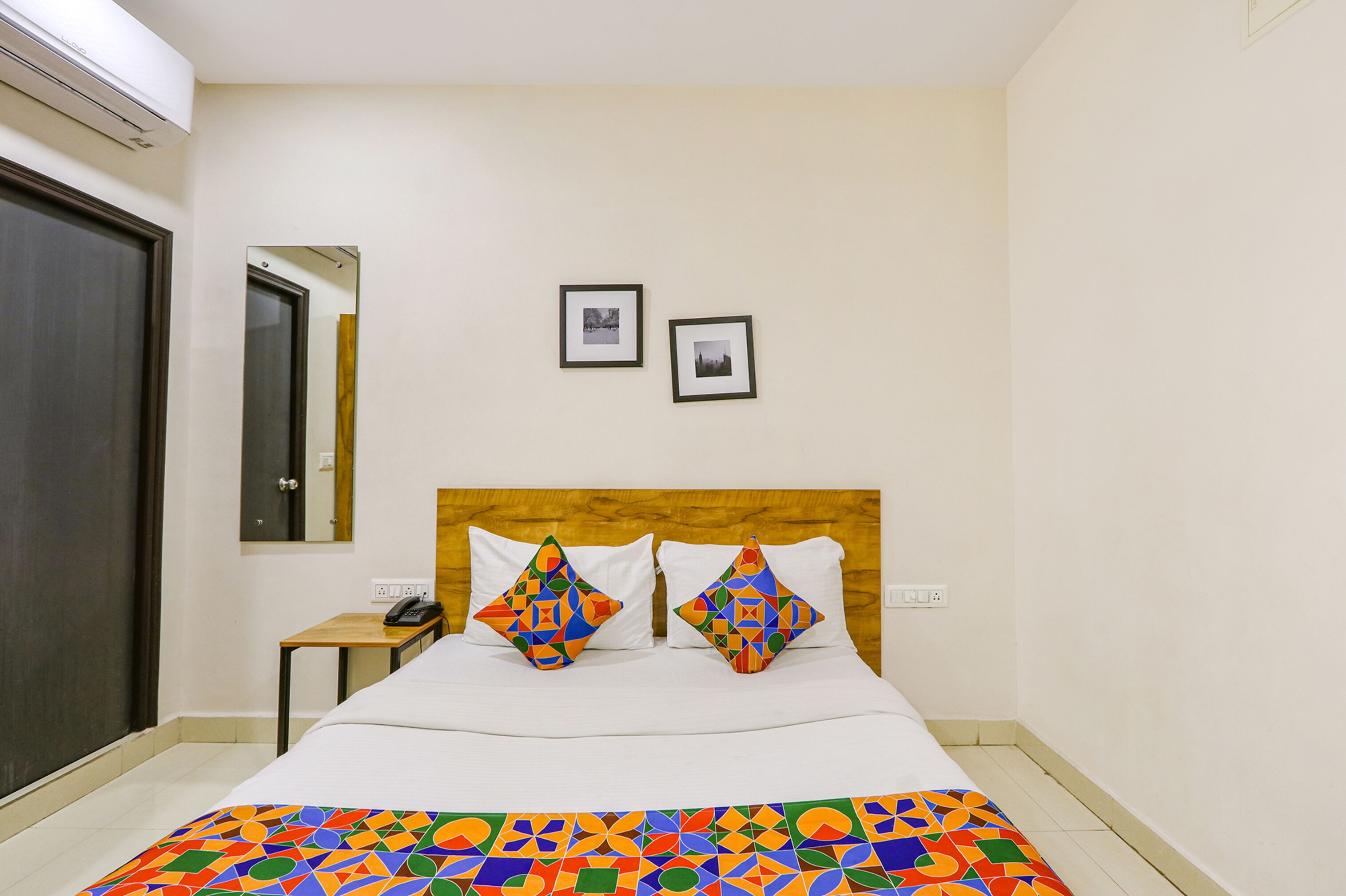 A hotel room with a bed, two pillows, a nightstand, a phone, and two framed pictures on the wall.