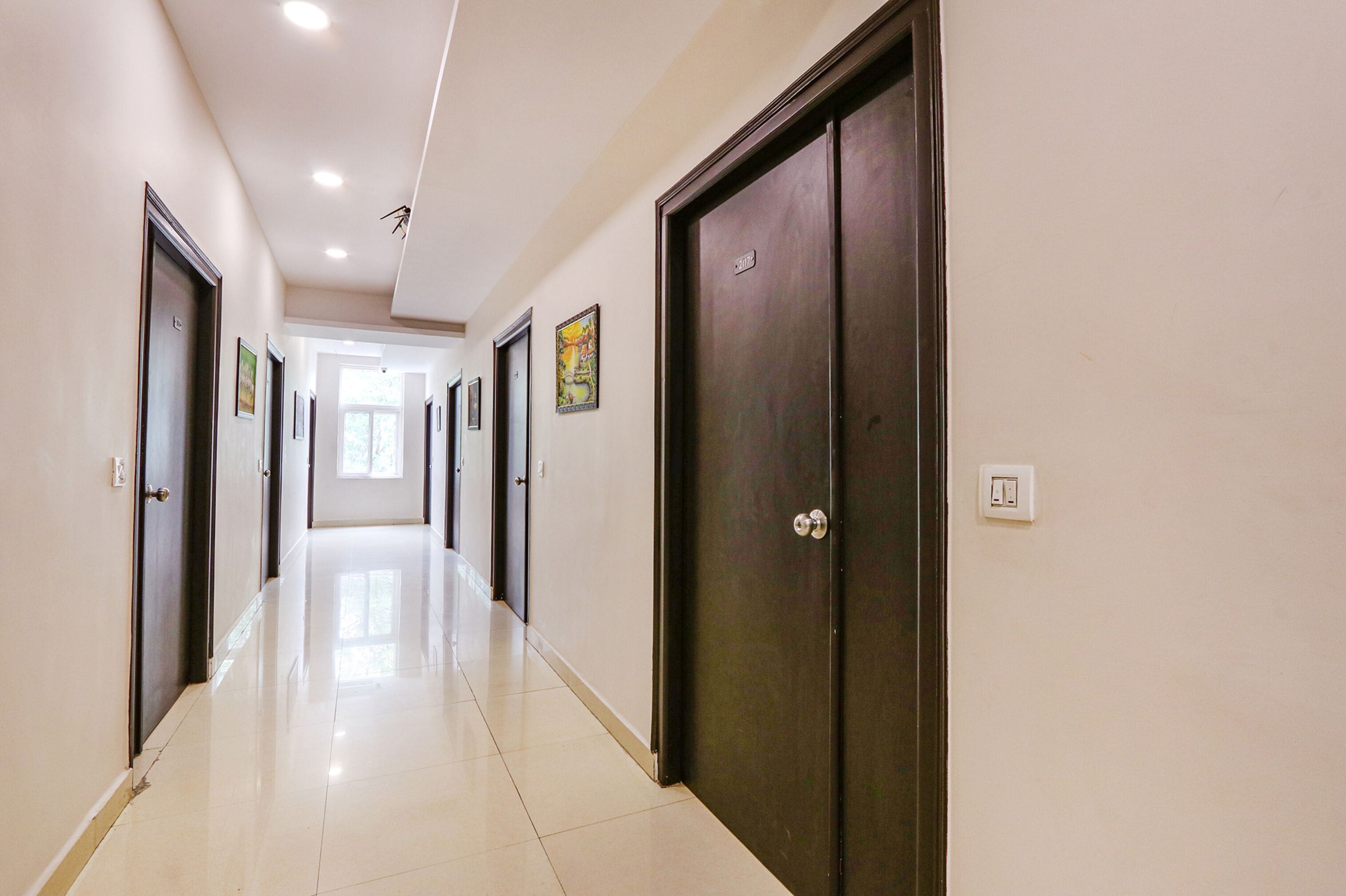 A hallway with doors on both sides, a tiled floor, and recessed ceiling lights.
