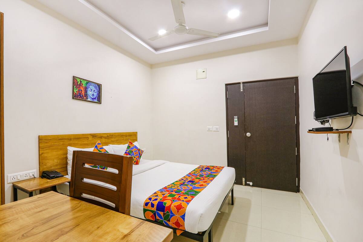 A hotel room with a bed, a wooden headboard, a bedside table with a phone, a TV on a shelf, and a door.