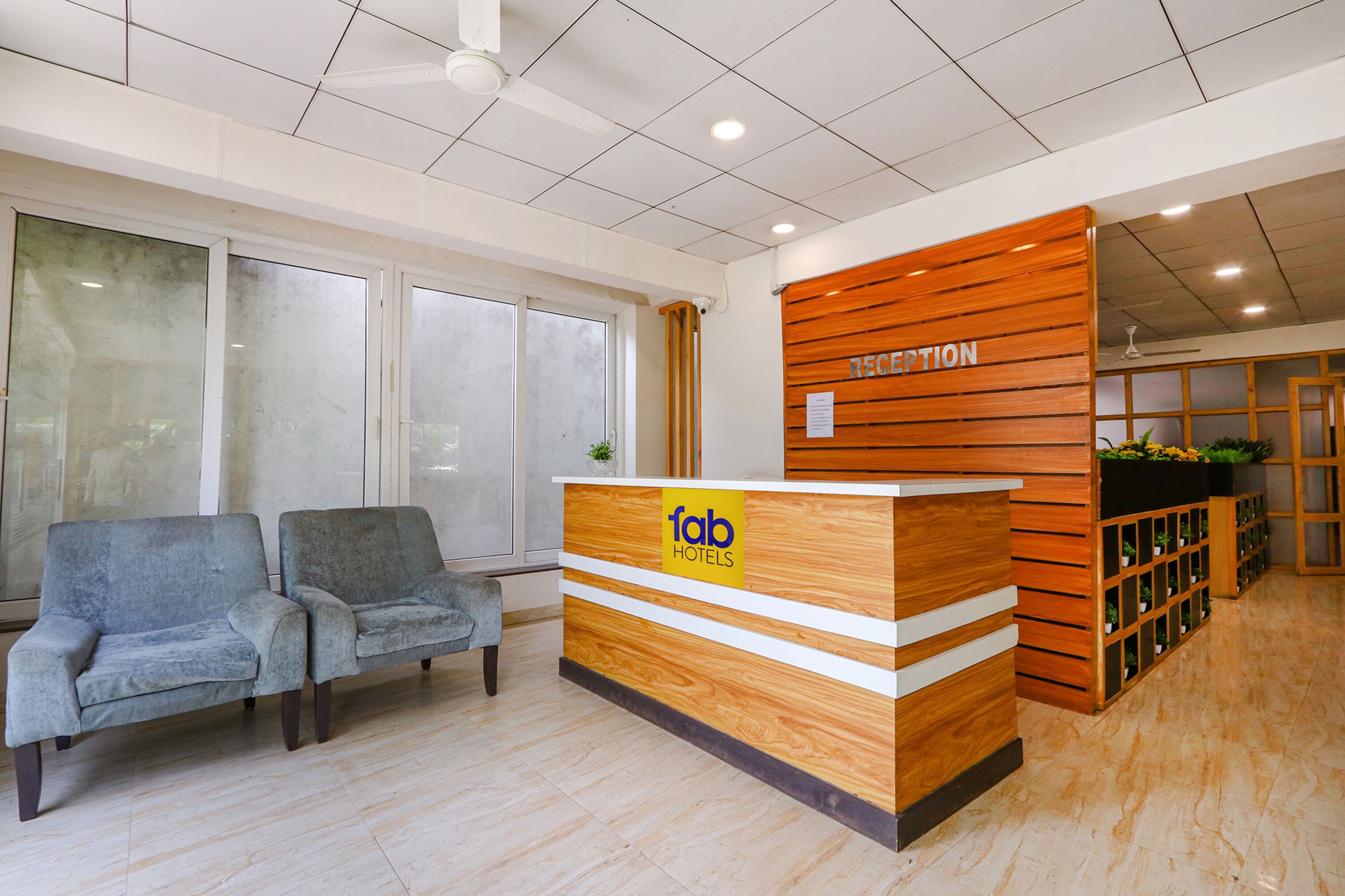A reception desk with a wooden finish and a sign reading "fab hotels". There are two grey upholstered chairs to the left of the desk.
