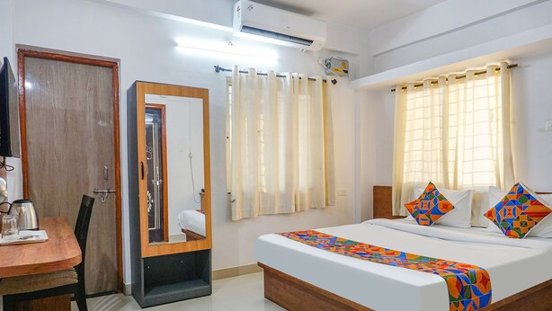 A hotel room with a bed, a desk, a chair, a mirror, and a window with curtains. - Fabhotel Lake View (Pune)