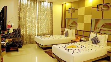 A hotel room with two beds, a large window with patterned curtains, a small table with a vase of flowers, and a mirror on the wall.