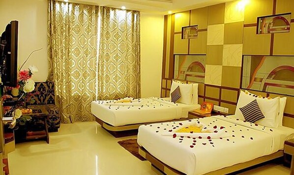 A hotel room with two beds, a large window with patterned curtains, a small table with a vase of flowers, and a mirror on the wall. - Fabhotel Prime Simna International (Muzaffarpur)