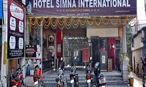 The entrance of Hotel Simna International with a signboard, a gated entrance, and parked motorcycles. - Fabhotel Prime Simna International (Muzaffarpur)