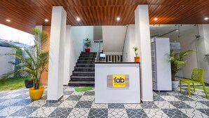 Zona de recepción de hotel con un diseño moderno, que incluye un techo de madera, un mostrador de recepción con un letrero de 'fab hotels' y plantas en macetas.