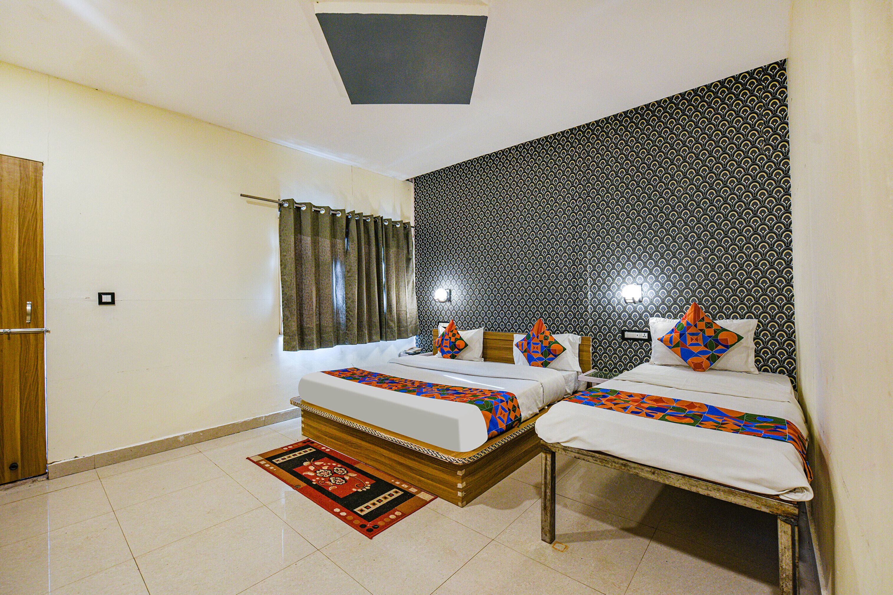 A double bed with a patterned bedspread, a wooden headboard, and a red and black area rug.