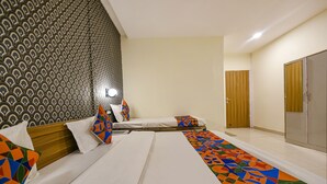 A hotel room with a patterned wall, a bed with colorful pillows, a bedside table with a lamp, and a large wardrobe. - Fabhotel Sizzling Resort & Adventure (Dhanaulti)