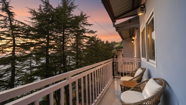 A balcony with wicker chairs and a table, overlooking a forested area during sunset. - Fabhotel Sizzling Resort & Adventure (Dhanaulti)