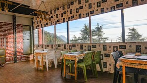 A dining area with a brick wall, large windows, and a view of mountains. - Fabhotel Sizzling Resort & Adventure (Dhanaulti)