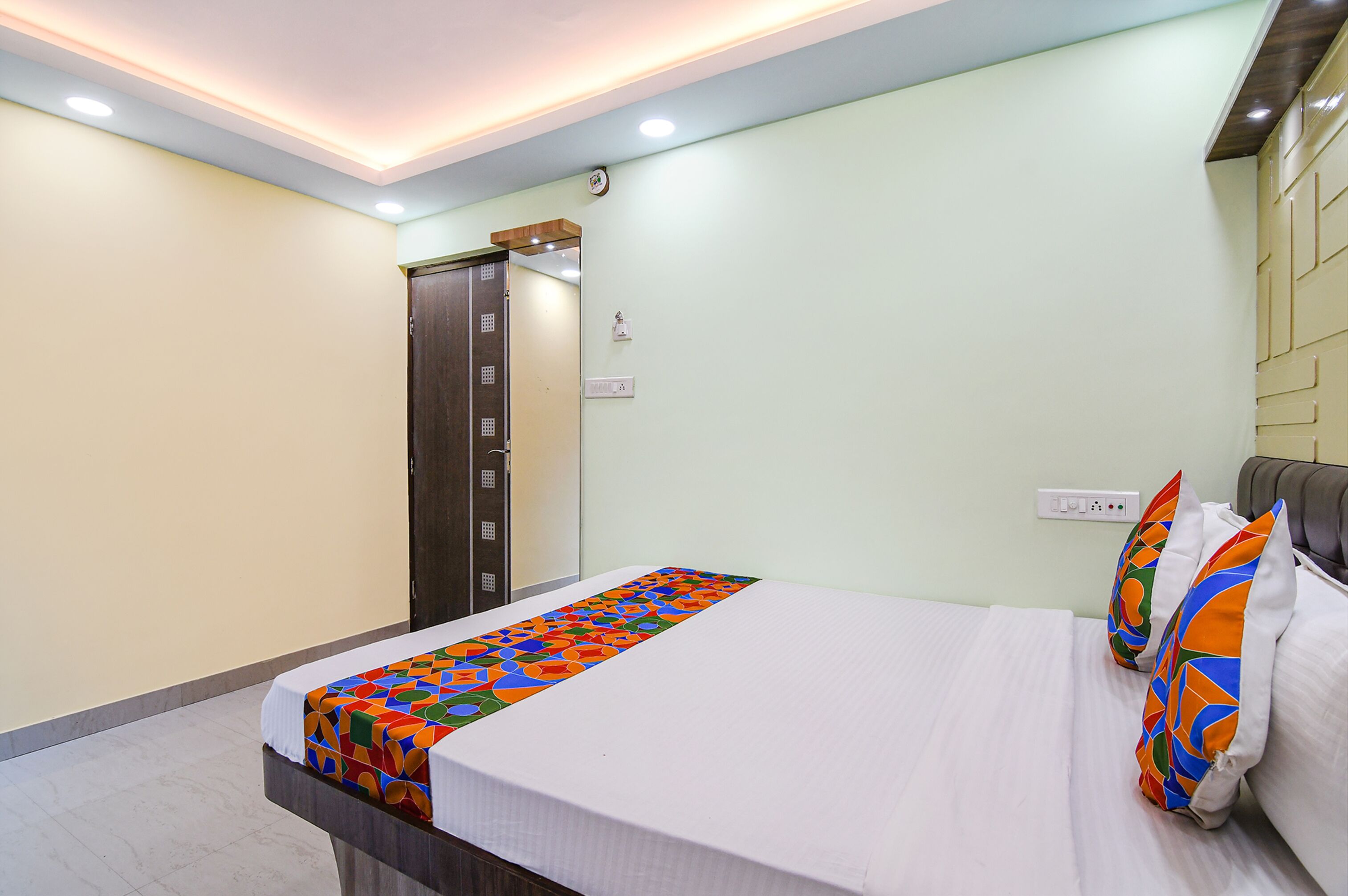 A hotel room with a bed, a bedside table, a wardrobe, and a wall-mounted light switch.
