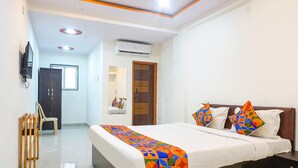 A hotel room with a bed, a TV, an air conditioning unit, a wooden wardrobe, and a small seating area with a chair and a sofa. - FabHotel Surya I Pune (Rajgurunagar)