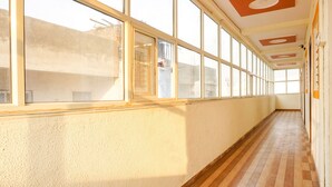 A long, narrow hallway with large windows on one side and a wooden floor. - FabHotel Surya I Pune (Rajgurunagar)
