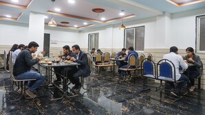 A dining area with tables and chairs, people eating, and a ceiling with recessed lighting. - FabHotel Surya I Pune (Rajgurunagar)