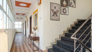 A hallway with wooden flooring, a desk with a vase, and a staircase with black steps and metal railings. - FabHotel Surya I Pune (Rajgurunagar)