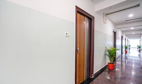 Corredor de hotel com porta de madeira, plantas em vasos e piso encerado.