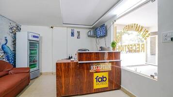 A reception desk with a 'fab hotels' sign, a peacock mural, a refrigerator, and a television on the wall.