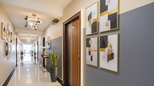 Een hotelgang met ingelijste kunstwerken, een potplant en een houten deur.