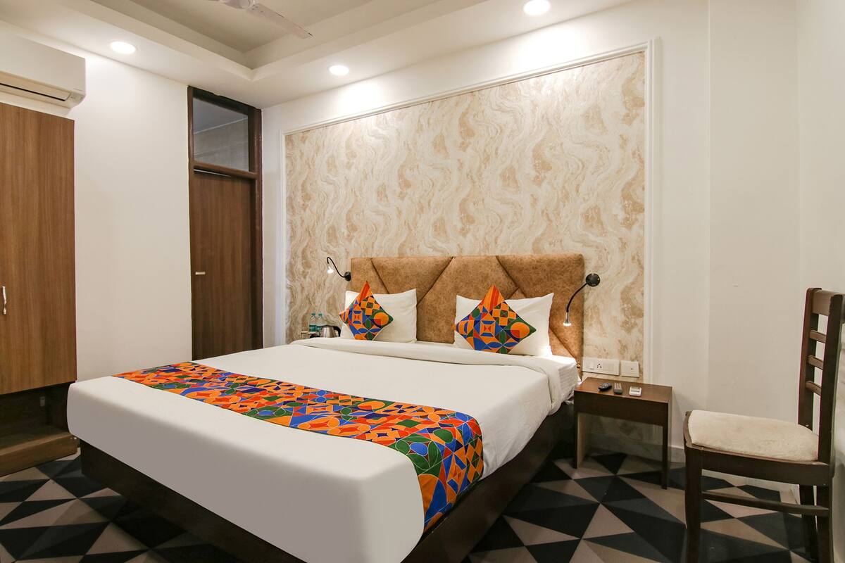 A hotel room with a large bed, a wooden headboard, a bedside table with a lamp, and a chair.