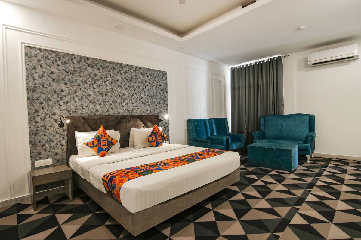 A hotel room with a bed, a nightstand, a blue armchair, and a patterned wall.