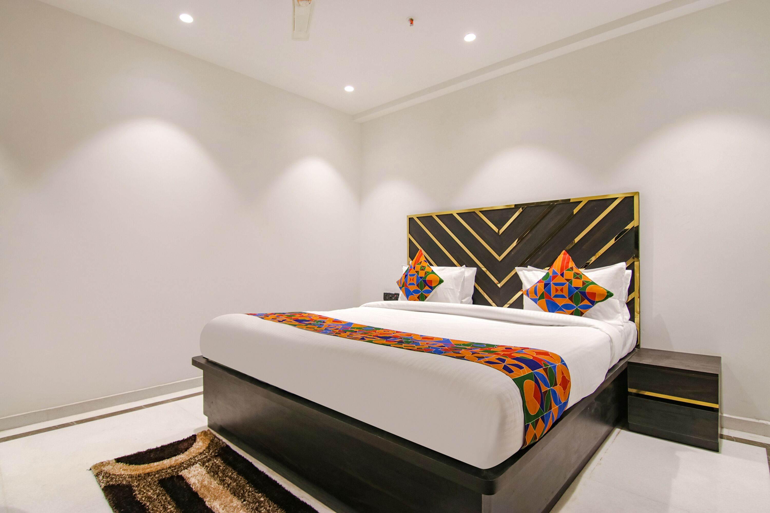 A modern hotel room with a large bed, a dark headboard, and a small bedside table.