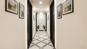 Un couloir aux murs ornés de tableaux encadrés, doté d’un sol carrelé et de plantes en pot à l’extrémité.
