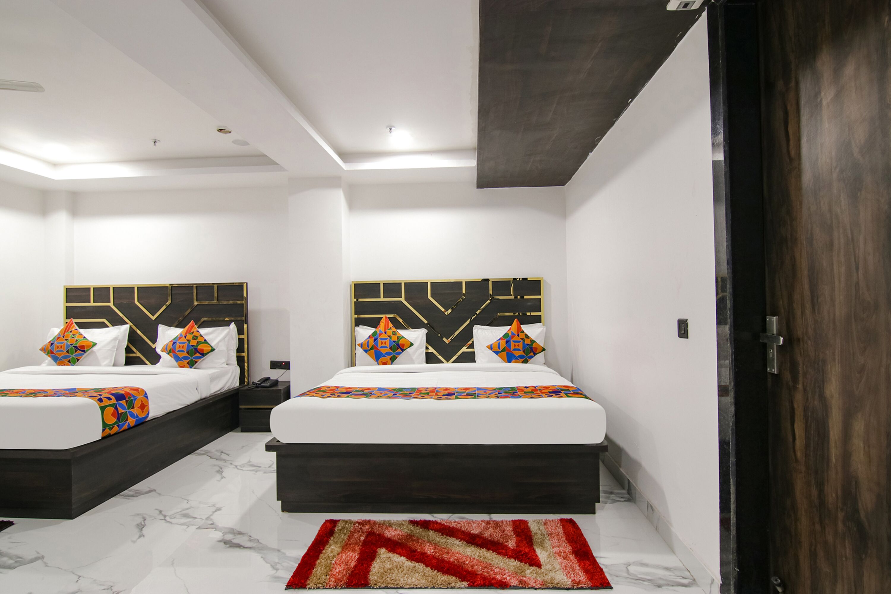 A modern bedroom with two beds, a dark headboard, and a red and beige rug.