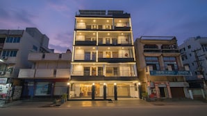 Un hôtel à plusieurs étages, doté de balcons, d’une entrée au rez-de-chaussée et d’une enseigne indiquant un commerce situé à proximité.