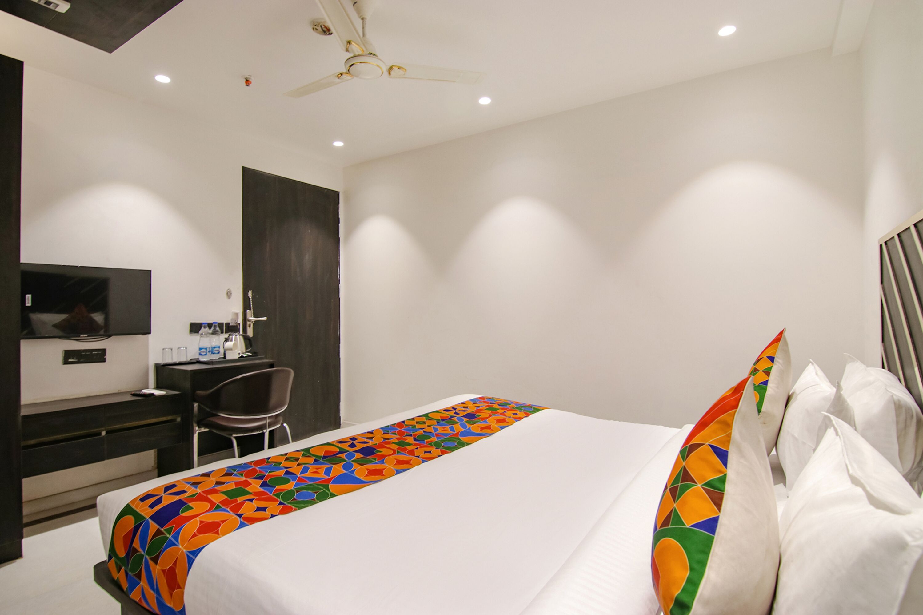 A hotel room with a bed, a desk, a chair, a television, and a ceiling fan.
