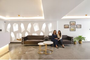 A modern lobby with a reception desk, a brown sofa, two round tables, and a potted plant. - FabHotel Sky Suites Karkardooma (New Delhi)