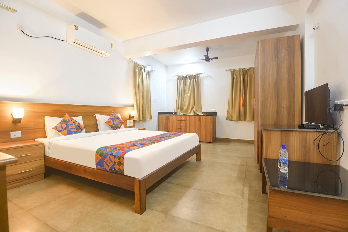 A hotel room with a bed, wooden wardrobe, desk, and a TV.