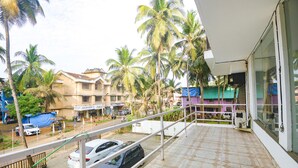 A balcony with a tiled floor, overlooking a street with parked cars and palm trees. - FabHotel Holiday Suites - Nr. Benaulim Beach (Benaulim)