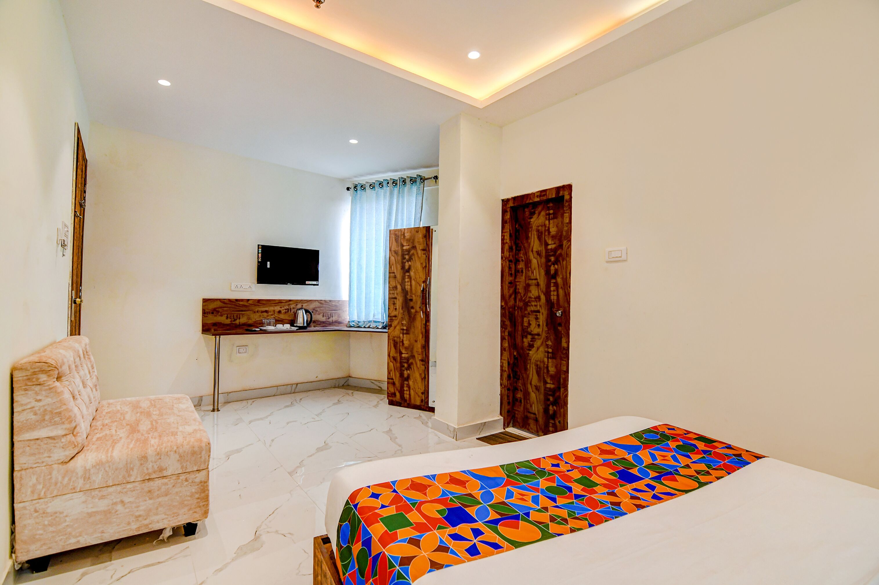 A hotel room with a bed, a sofa, a desk with a TV, and a window with curtains.