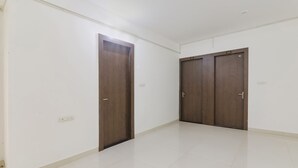 A hallway with two wooden doors, white walls, and a tiled floor. - Fabhotel The Villa I (Prayagraj)