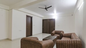 A spacious living room with a ceiling fan, a coffee table, and brown upholstered furniture. - Fabhotel The Villa I (Prayagraj)