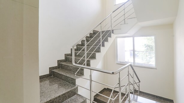 A staircase with metal railings and granite steps, leading to a landing with a large window. - Fabhotel The Villa I (Prayagraj)