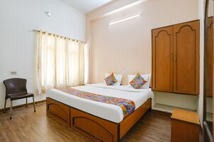 Quarto com cama de madeira, uma cadeira, um guarda-roupa e uma janela com cortinas.