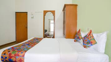 A hotel room with a bed, a wooden wardrobe, a mirror, and a door.