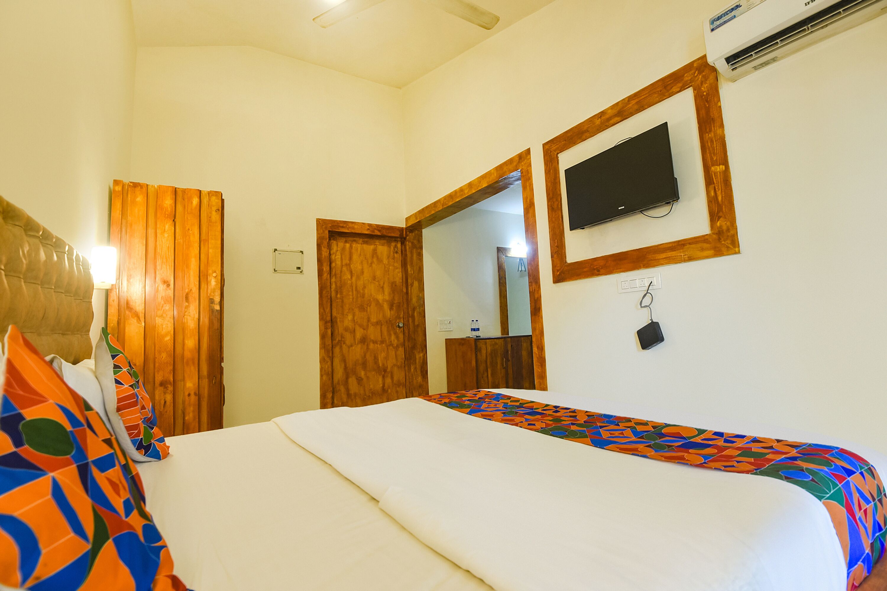 Habitación de hotel con cama, puerta de madera y televisor montado.