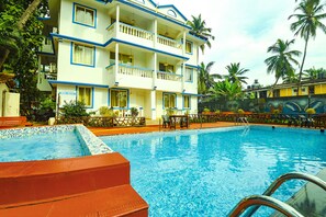 Ett hotell med en swimmingpool, flera balkonger och palmer.