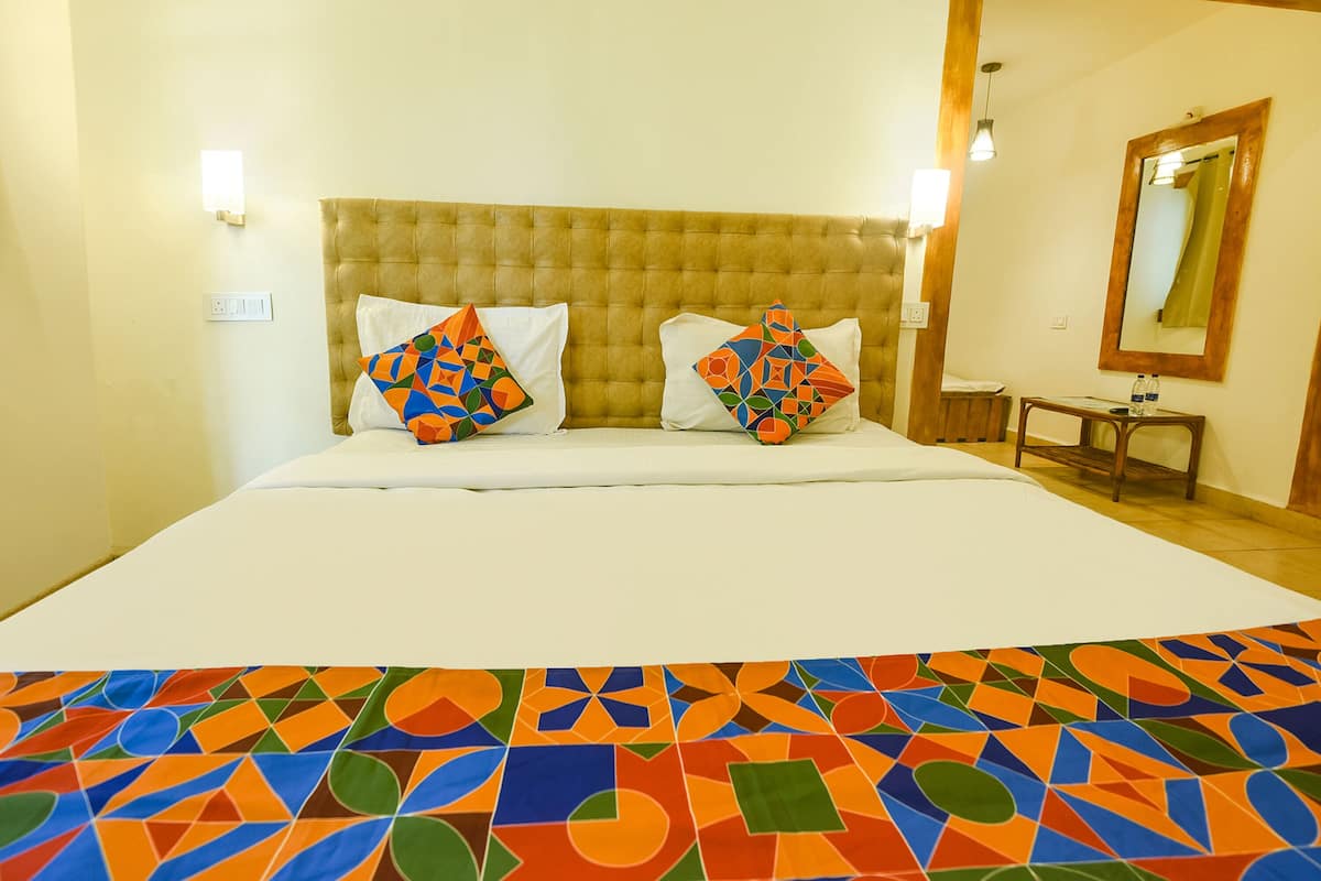 Ein Hotelzimmer mit einem großen Bett, zwei Kissen mit farbenfrohen geometrischen Mustern, einem hölzernen Kopfteil, einem Nachttisch mit Spiegel und einer Wandleuchte.