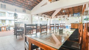 A restaurant with wooden tables and chairs, a glass-top table, and a ceiling with wooden beams. - Fabhotel Grand Royal Palms (Benaulim)