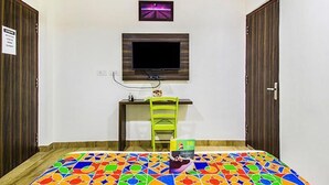 Une pièce comprenant un lit, un bureau, une chaise, un téléviseur fixé au mur et un tapis coloré.