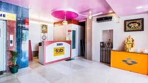 Un hall d’hôtel avec un comptoir d’accueil, un grand luminaire rose au plafond et une statue de Bouddha sur la droite.