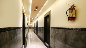 A long, well-lit hallway with marble walls and doors, a fire extinguisher mounted on the wall, and a tiled floor. - Fabhotel Sai Vihar (Thane)